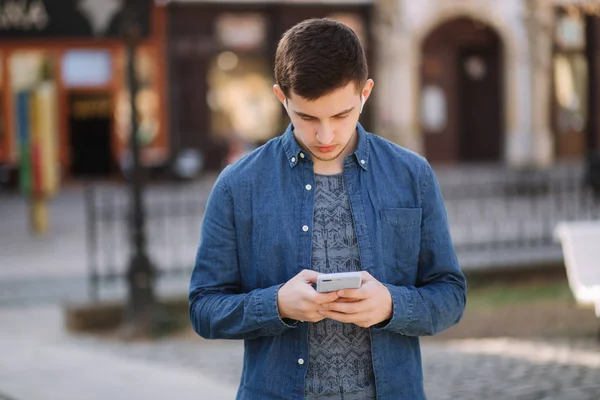 Young man use phone and wireless headphones and print message in social network. Male blogger — Stock Photo, Image