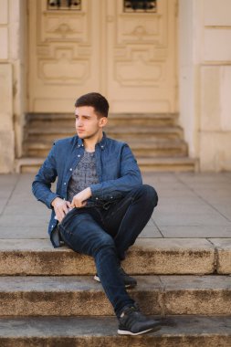 Park yakınında merdivenlerde sitiing yakışıklı adam ve kablosuz kulaklıklar için kapak çıkarmak için bir cep içine el koydu