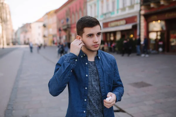 Mann setzte seine drahtlosen Kopfhörer auf. schöner Mann in blauem Hemd stehen in der Mitte, wenn die Stadt — Stockfoto