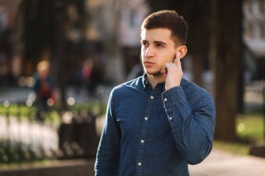 Yakışıklı adam kablosuz kulaklıklar üzerine parmağını koydu ve konuşuyor. Adam portresi telefonla konuşma yapar