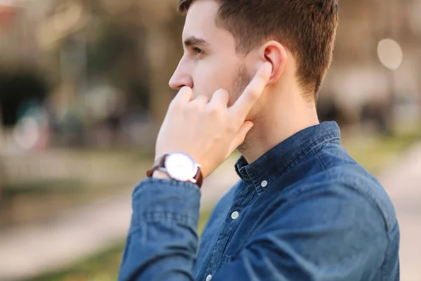 Handsome man put his finger on wireless headphones and speaks. Portrait of man makes conversation by the phone — Stock Photo, Image