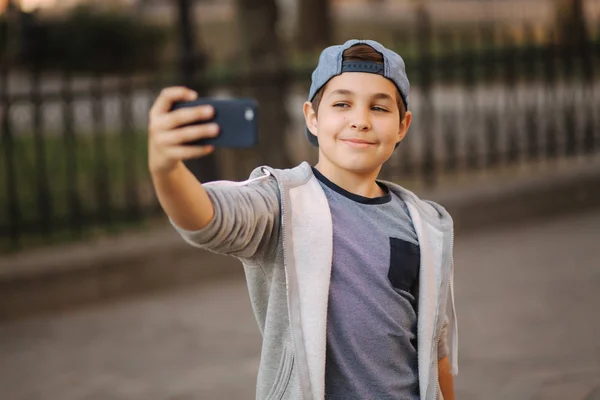 Junge macht ein Selfie mit Smartphone in der Innenstadt. Netter Junge mit blauem Hut. Stilvoller Schuljunge — Stockfoto