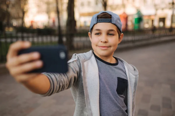 Giovane ragazzo fare un selfie su smartphone nel centro della città. Bel ragazzo col cappello blu. Elegante ragazzo della scuola — Foto Stock