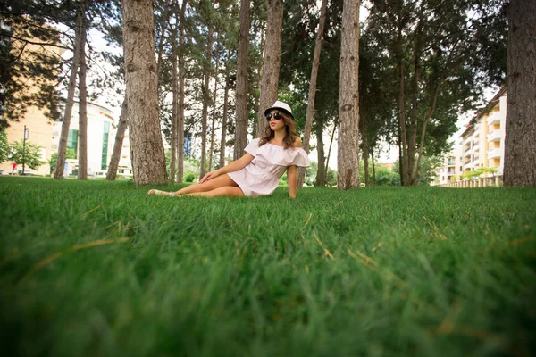 Menina bonita em vestido e chapéu no parque. Grama verde e ensolarado. Contexto das árvores — Fotografia de Stock
