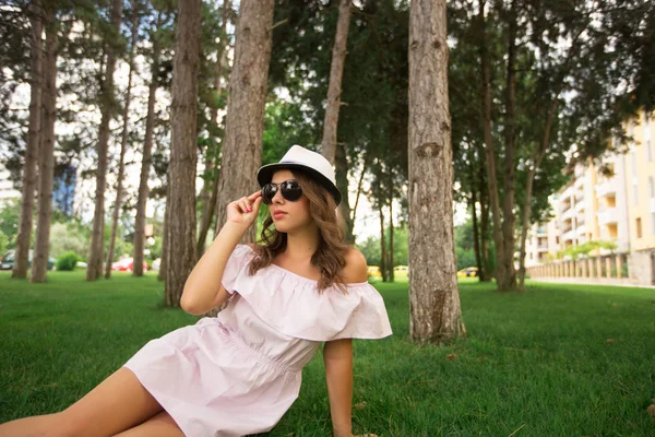Mooi meisje in de kleding en hoed in het park. Groen gras en zonnig. Achtergrond van bomen — Stockfoto