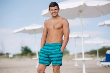 Plajdaki şortlu adam. Güneş gözlerinin içine parlar ve o şaşı