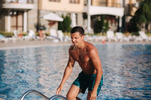 Όμορφος άντρας πάει έξω από την πισίνα. Νέος άνθρωπος με πράσινα σορτς κολύμβησης από το ξενοδοχείο — Φωτογραφία Αρχείου