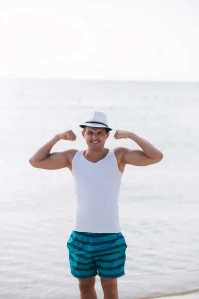 Boldog ember megmutatja a bicepsz a tenger előtt. Fiatal férfi séta a strandon — Stock Fotó