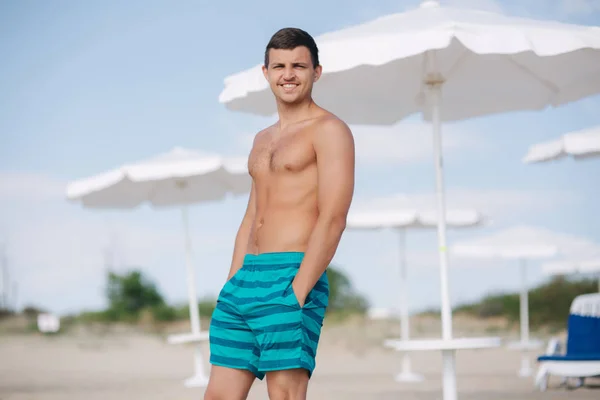穿短裤的男人站在海滩上。阳光照在他的眼睛里, 他斜视着 — 图库照片
