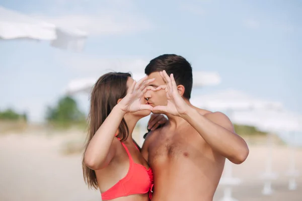 Una pareja feliz hace un corazón. Mujer y hombre en la playa. Se besan — Foto de Stock