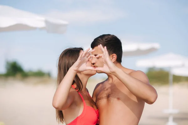 Un couple heureux fait un cœur. Femme et homme sur la plage. Ils s'embrassent — Photo