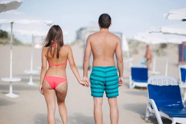 Back couple walking on the beach. On the back of a man and on the womans buttocks is handprint of sand