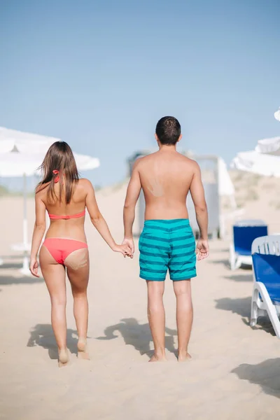 Back couple walking on the beach. On the back of a man and on the womans buttocks is handprint of sand