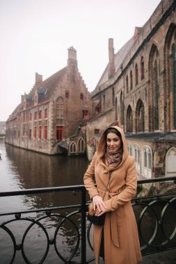 Bealgium, Brugge köprüsünde kahverengi ceket ayakta güzel kadın portresi. Kadın bir Hood koymak