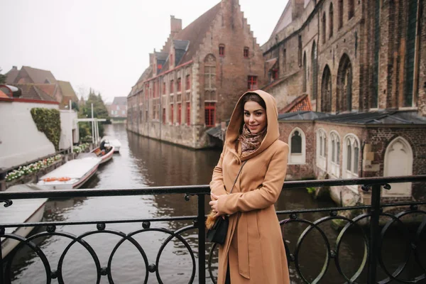 Bealgium, Brugge köprüsünde kahverengi ceket ayakta güzel kadın portresi. Kadın bir Hood koymak