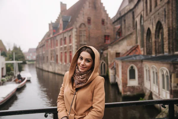 Retrato de mulher bonita de casaco marrom em pé na ponte em Bealgium, Brugge. Feminino colocar em um capuz — Fotografia de Stock