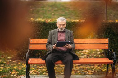 Büyükbaba bankta parkta oturan bir tablet kullanır