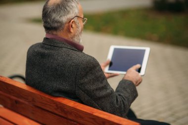 Büyükbaba bankta parkta oturan bir tablet kullanır