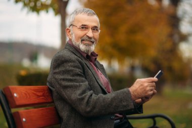 Büyükbaba bankta parkta oturan bir tablet kullanır