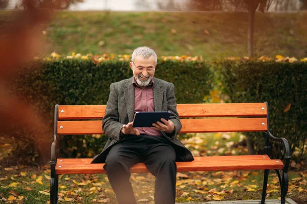 할아버지는 벤치에 공원에 앉아 태블릿을 사용 — 스톡 사진
