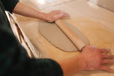 Erkek çömlekçi kil için rollong pin kullanır. Atölyedeki adam