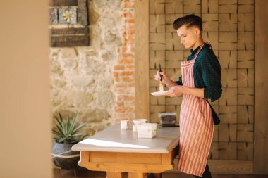 Young artist making ornament on ceramic plate. Handsome young man working at his workshop