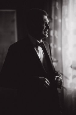 Mutlu damat evdeki pencerenin yanında duruyor. Damat sabahı. Takım elbiseli yakışıklı adam