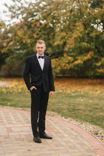 秋に外に立つ黒いスーツを着たハンサムな男。花嫁を待っている新郎 — ストック写真