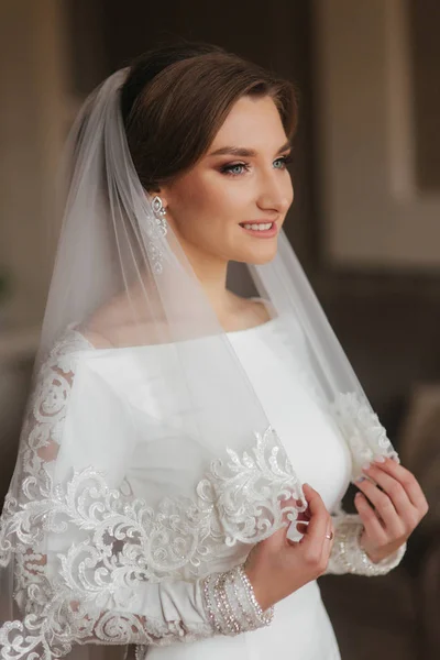 Retrato de noiva bonita em pé junto à janela em casa. Noiva encantadora em vestido de casamento branco — Fotografia de Stock