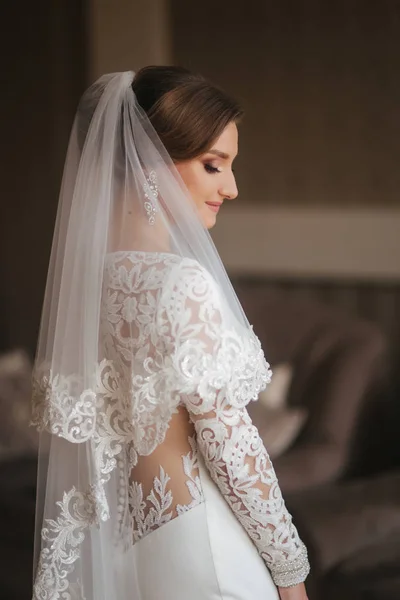 Retrato de noiva bonita em pé junto à janela em casa. Noiva encantadora em vestido de casamento branco — Fotografia de Stock