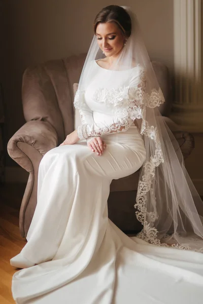 Linda noiva sentada na cadeira em casa. Mulher bonita em vestido de noiva — Fotografia de Stock