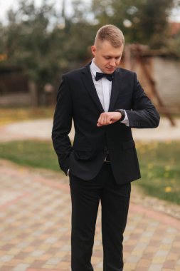 Takım elbiseli yakışıklı adam dışarıdaki saate bak, sonbahar. Güzel kravat yay ile siyah takım elbiseli adam