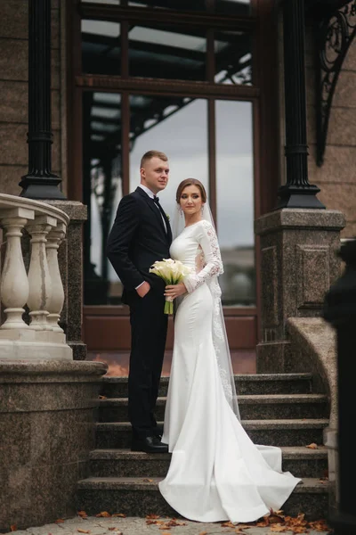 Casal elegante fica nas escadas perto do palácio. Bonito noivo e noiva linda no casamento — Fotografia de Stock