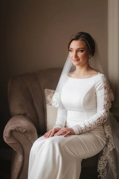 Linda noiva sentada na cadeira em casa. Mulher bonita em vestido de noiva — Fotografia de Stock