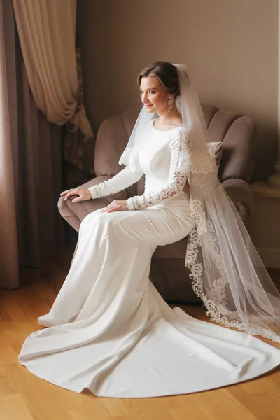 Linda noiva sentada na cadeira em casa. Mulher bonita em vestido de noiva — Fotografia de Stock