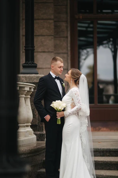 Casal elegante fica nas escadas perto do palácio. Bonito noivo e noiva linda no casamento — Fotografia de Stock