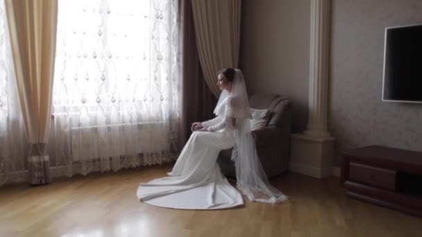 Gyönyörű menyasszony ül a széken, az otthon. Gyönyörű nő a menyasszonyi ruha — Stock videók