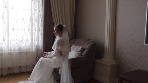 Hermosa novia sentada en la silla de la casa. Hermosa mujer en vestido de novia — Vídeos de Stock