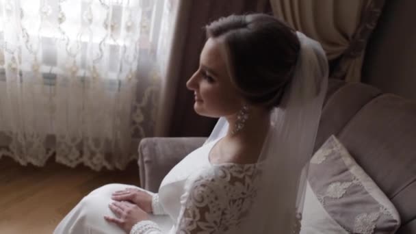 Gorgeous bride sitting on the chair at the home. Beautiful woman in wedding dress — Stock Video