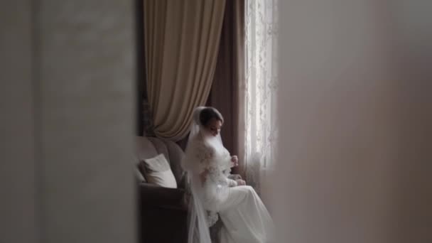 Hermosa novia sentada en la silla de la casa. Hermosa mujer en vestido de novia — Vídeos de Stock