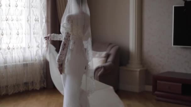 Красивая невеста крутится в свадебном платье дома. Фон большого окна — стоковое видео