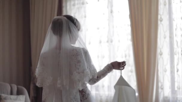 Красивая невеста крутится в свадебном платье дома. Фон большого окна — стоковое видео