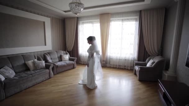 Όμορφη νύφη στριφογυρίζει στο νυφικό στο σπίτι. Φόντο μεγάλου παραθύρου — Αρχείο Βίντεο