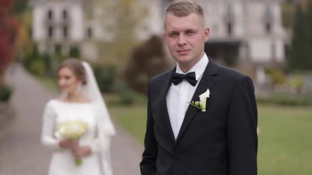 Sposo e sposa passeggiando nel parco vicino a un grande palazzo. Bello uomo e bella donna — Video Stock