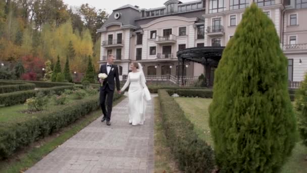Молодая пара в свадебном платье гуляет по парку — стоковое видео