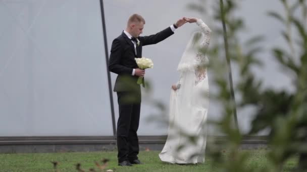 Ženich venku se točí kolem nevěsty. Pozadí velkého okna — Stock video