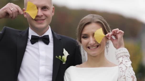 Ο γαμπρός και η νύφη βάζουν κίτρινα φύλλα στα μάτια. Φθινοπωρινό πάρκο — Αρχείο Βίντεο