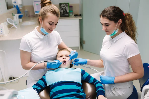 Детский дантист и ассистент осмотра зубов мальчиков, в то время как он сидит на стоматологическом стуле в офисе. Женщина-дантист — стоковое фото