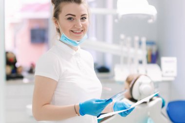 Klinikte genç diş hekimi ekipman ve gülümseme önünde standı