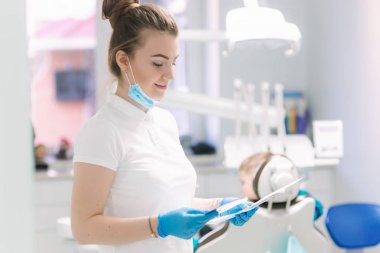 Klinikte genç diş hekimi ekipman ve gülümseme önünde standı